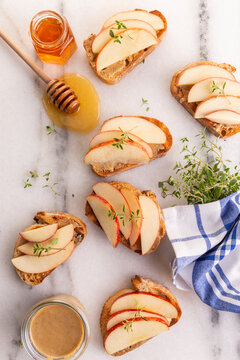 Snacks Made Of Toast With Nut Butter, Apple And Honey On A Marble Background With Thyme Sprigs