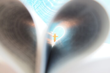 Wood crucifix in light, behind blurred heart shape bible page on blue background. Easter, hope, faith, love, symbol christianity, religious Christian image, study church online, Jesus loves you.