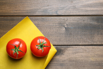 Fresh ripe tomatoes and waxed napkin on wooden table, top view. Space for text