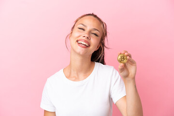 Teenager Russian girl holding a Bitcoin isolated on pink background laughing