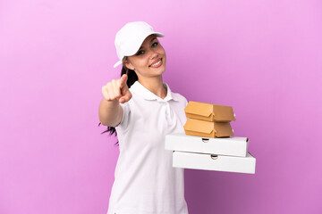 Pizza delivery Russian girl with work uniform picking up pizza boxes and burgers isolated on purple...