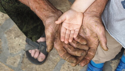 The hand of a child lies on the hand of a working man. Communication and continuity of two...