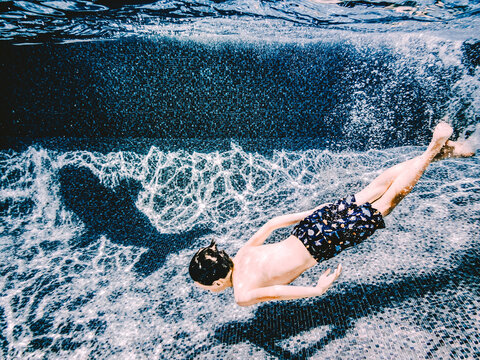 8 years old boy swimming with the shadow of a dolphin in a pool