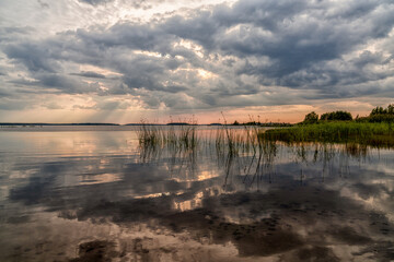 colorful sunset and expressive sky reflections in a calm and peaceful lake with reeds in the foreground