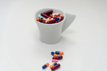 Un vaso blanco lleno de pastillas de colores sobre fondo blanco. 