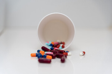 píldoras de colores en un vaso de papel blanco tiradas sobre fondo blanco
