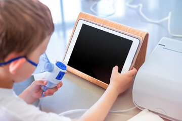 The boy breathes through the mask, inhales and looks into the tablet