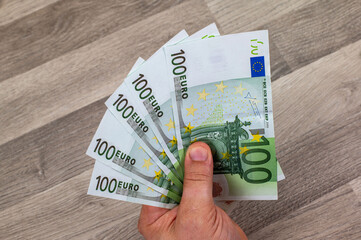 man's hand holding fanned 100 euro banknotes