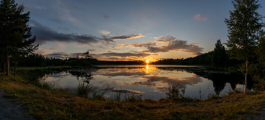 Obraz premium panorama of a colorful sunset reflected in a calm lake landscape with green forest and reeds