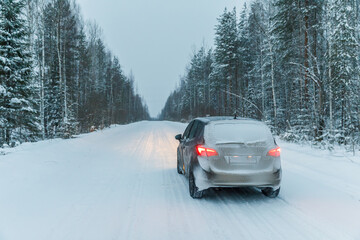 Car on winter road with ice on the asphalt, trees under snow during the winter frost in Russia.