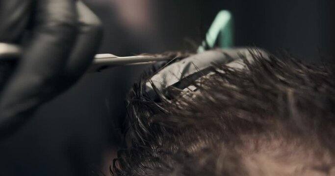 Barber hands cutting hair of man using comb and scissors at salon