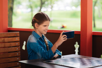 Close-up portrait of a girl behind a smartphone, a schoolboy communicates on a smartphone. Cute girl typing on the phone against green background outdoors.
