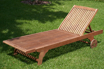 Wooden chaise longue in the fresh garden on the green grass. The shadow of a tree on the grass.The...