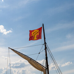 flag of the Finnish city of Vaasa flying in a strong wind from the mast of an old sailboat under a...