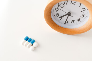 Alarm clock and white blue pills on white table background.
