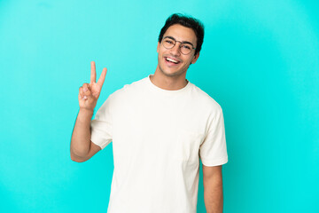 Fototapeta premium Caucasian handsome man over isolated blue background smiling and showing victory sign