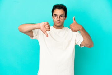 Fototapeta premium Caucasian handsome man over isolated blue background making good-bad sign. Undecided between yes or not