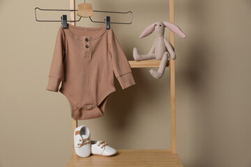 Baby bodysuit, shoes and toy bunny on chair near beige wall