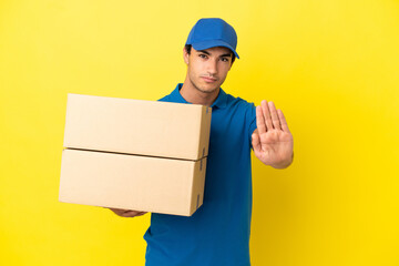 Delivery man over isolated yellow wall making stop gesture