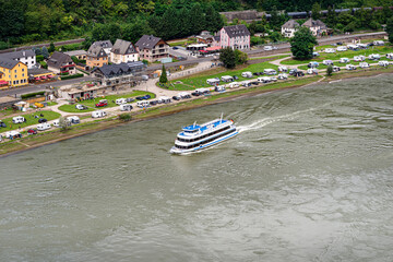 Obraz premium A tourist ship sailing on the river Rhine in western Germany, visible buildings and caravans on the river bank.