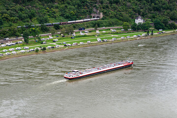 A tanker barge sailing on the river Rhine in western Germany, visible buildings and caravans on the river bank, aerial view.