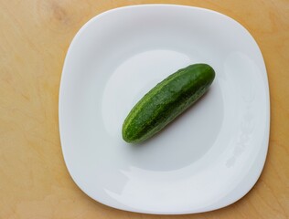 Green appetizing cucumber on a white glossy plate. Top view - flatlay