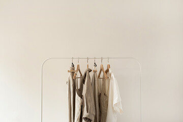 Minimal aesthetic fashion clothes concept. Neutral beige washed linen female blouses, dresses and t-shirts on hanger on white background. Fashion blog, website, social media