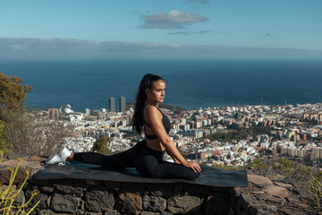 photograph of a girl in black sportswear practicing yoga and sports outdoors with beautiful views behind her