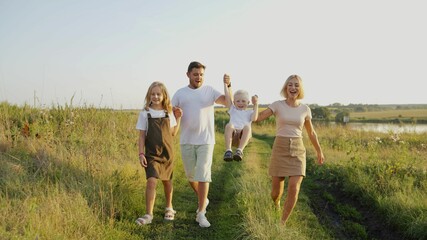 Summer vacation concept. Day of mother, father, child. Family spending time together in nature. Family holding hands. Mom, dad, son and daughter are walking in a summer meadow. Dad, mom, kids at