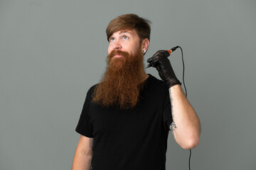 Tattoo artist redhead man isolated on blue background and looking up