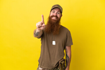 Redhead Military man with dog tag isolated on yellow background showing and lifting a finger
