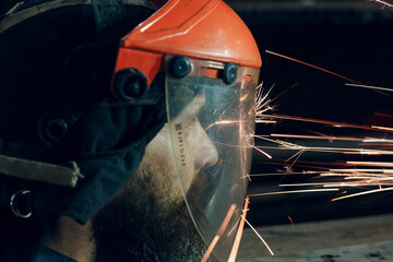 Man worker in transparent protective mask works on metal with circular grinder saw. Sparks and face