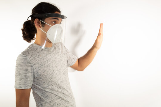 Hispanic Man With Long Hair Wearing A Kn95 Face Mask And A Face Shield Against A White Background Showing Protection Measures Against Covid