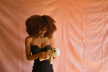 Young Latina woman in black dress sticking a pin in the heart of a voodoo doll while smiling on a...