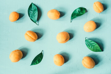 Top view of ripe apricots and leaves scattered on green plastered surface.