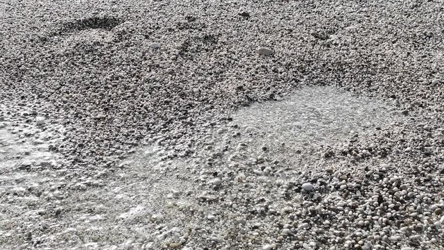 Slow motion of gentle waves washing over foot prints on a pebble beach.