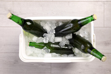 Plastic cool box with ice cubes and beer on wooden floor, top view