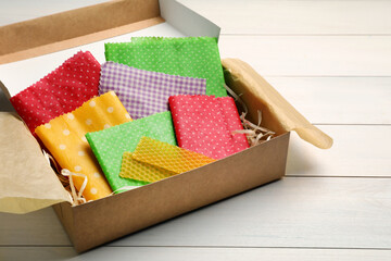 Colorful beeswax food wraps in box on white wooden table