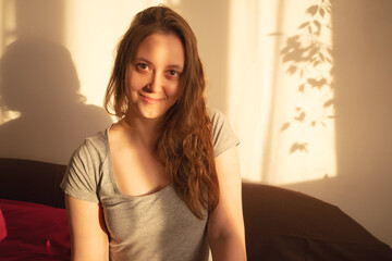 Young woman looking at camera in warm rays of sunset. Warm calm portrait of girl indoor. light and shadow on the face