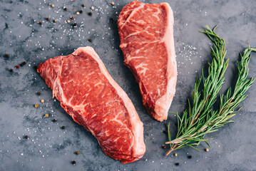 Raw New York striploin beef steak isolated on gray background with rosemary and spices