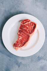 Raw New York striploin beef steak in white plate on blue background