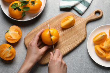 Woman cutting fresh ripe yellow tomato at light grey table, top view