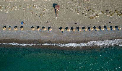 Aerial view from a flying drone of beach umbrellas in a row on an empty beach with braking waves.