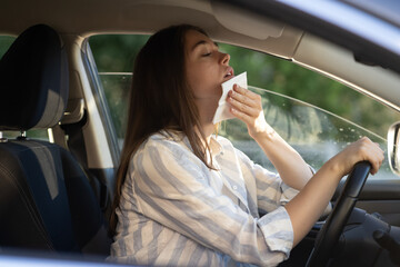 Young woman sweating tired of heat driving car hold tissue at face. Girl driver in vehicle suffer...