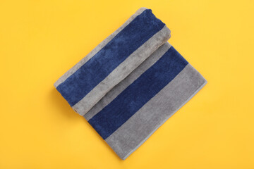 Rolled striped beach towel on yellow background, top view