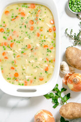 Homemade chicken and dumplings with carrots, peas and potatoes in a white baking dish