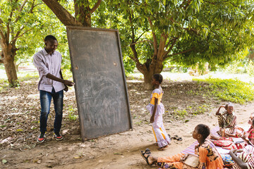 Tall black teacher in casual clothing inviting one of his small pupils to write something on the...