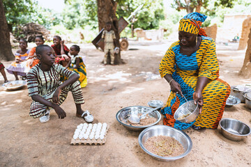 Smiling black African women sitting on a small chair, dividing her family's meal, with her son...