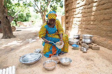 Attentive black housewife sitting in her outdoor kitchen in a typical rural Afriacn courtyard,...