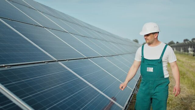 Engineer is checking the operation of sun and cleanliness of photovoltaic solar panels. Concept renewable energy. Caucasian man in hard helmet examining object solar panels. Concept of green energy
